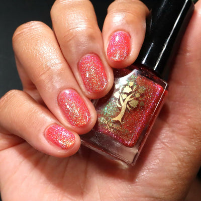 Protector of the Deep by Danglefoot Nail Polish, orange-pink reflective shimmer glitter bottle held in a light-medium hand