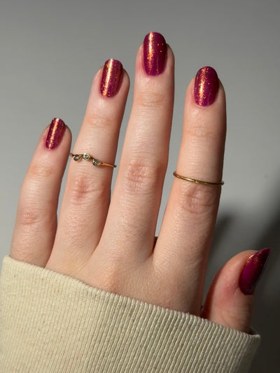 Should I Stay by Dam Nail Polish, deep fuchsia-berry jelly with warm gold and orange-shifting multichrome shimmer, on a light skin tone hand