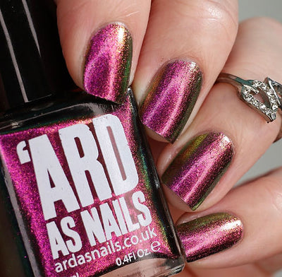 Joyeau by 'Ard As Nails, gold-pink multichrome chrome showing full range from vivid magenta-pink to olive-gold in bright daylight, bottle held in a light skin tone hand