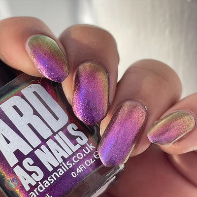 Thorn by 'Ard As Nails, multichrome chrome shifting between magenta-purple, warm gold, and deep red across angles in bright daylight, on a light-medium skin tone hand