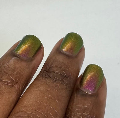 Joyeau by 'Ard As Nails, gold-pink multichrome chrome showing olive-green to golden amber to pinkish-magenta shift across nail surface in bright daylight, on a deep skin tone hand