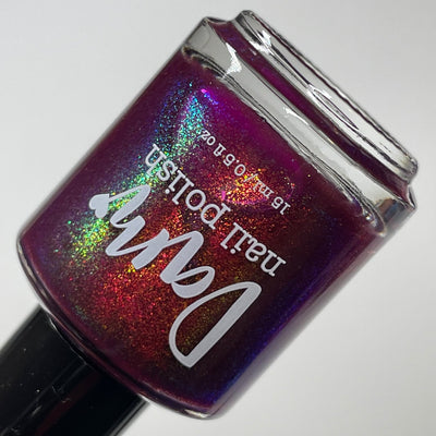 Should I Stay by Dam Nail Polish, deep fuchsia-plum jelly with gold-to-teal multichrome shimmer reading near-holographic under direct flash, bottle standalone product shot