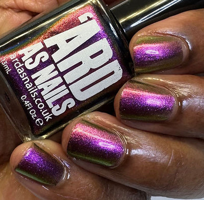 Joyeau by 'Ard As Nails, gold-pink multichrome chrome mid-shift from vivid violet-purple to olive-gold under direct flash, bottle held in a deep skin tone hand