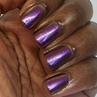Thorn by 'Ard As Nails, magenta-purple multichrome chrome with red-pink and gold colour-shifting shimmer in bright daylight, on a deep skin tone hand