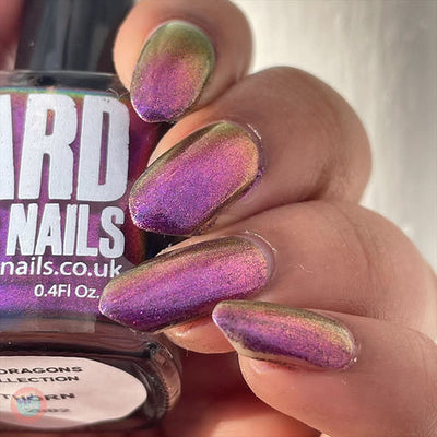Thorn by 'Ard As Nails, multichrome chrome shifting between magenta-purple and gold-green depending on angle in bright daylight, bottle held in a light skin tone hand