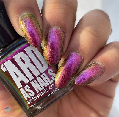 Joyeau by 'Ard As Nails, gold-pink multichrome chrome shifting deep magenta-pink to reddish-gold with olive-gold at the edges, bottle held in a medium skin tone hand