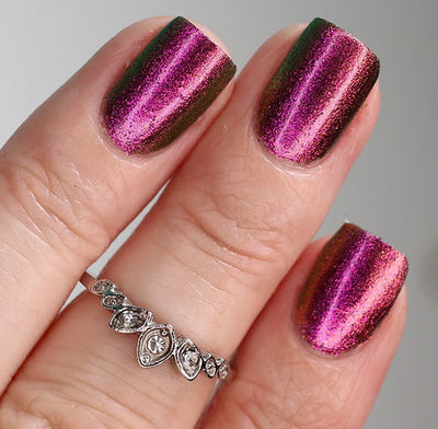 Joyeau by 'Ard As Nails, gold-pink multichrome chrome with linear stripe highlight pattern shifting magenta-pink through reddish-brown to olive-green, on a light skin tone hand