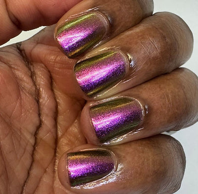 Joyeau by 'Ard As Nails, gold-pink multichrome chrome shifting olive-gold to vivid violet-magenta across nail angles, on a rich skin tone hand