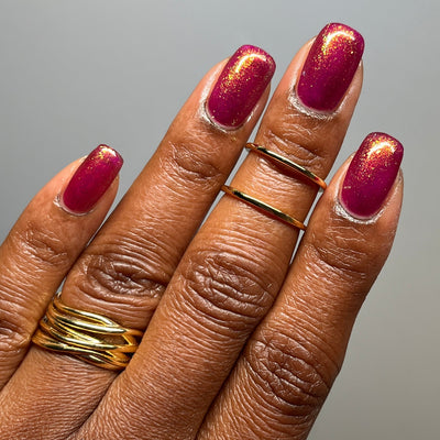 Should I Stay by Dam Nail Polish, deep fuchsia jelly with intense gold and warm amber multichrome shimmer, on a deep skin tone hand
