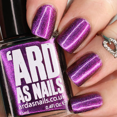 Thorn by 'Ard As Nails, deep magenta-purple chrome with distinct linear magnetic striping and bright reflective highlights, bottle held in a light skin tone hand