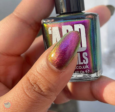 Joyeau by 'Ard As Nails, gold-pink multichrome chrome showing magenta-pink to reddish-gold shift with fine holographic sparkle, bottle held in a light-medium skin tone hand