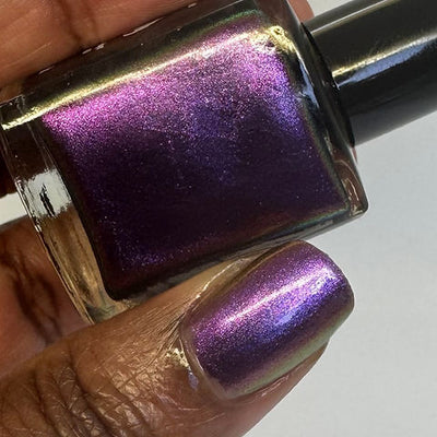 Thorn by 'Ard As Nails, multichrome chrome shifting between magenta-purple, bright pink, and gold under direct flash, bottle held in a deep skin tone hand