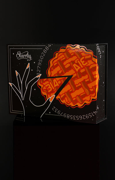 Pi Day Gift Set (Limited Edition) by Starrily, matte black collector's box with gloss orange lattice pie illustration and pi digits, in lifestyle setting