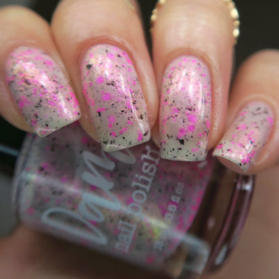 Shimmer Storm by Dam Nail Polish, milky greige-white base loaded with neon magenta-pink and dark black glitters with soft pink-gold shimmer, on a light skin tone hand