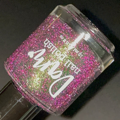 Snake by Dam Nail Polish, black jelly with pink-magenta and olive-green multichrome reflective glitter under direct flash, bottle standalone product shot