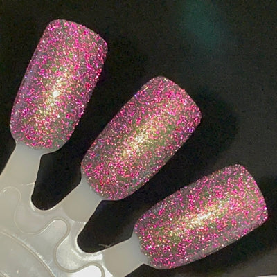 Snake by Dam Nail Polish, black jelly showing dense hot pink and magenta reflective glitter with olive-green multichrome shift under direct flash, swatch stick