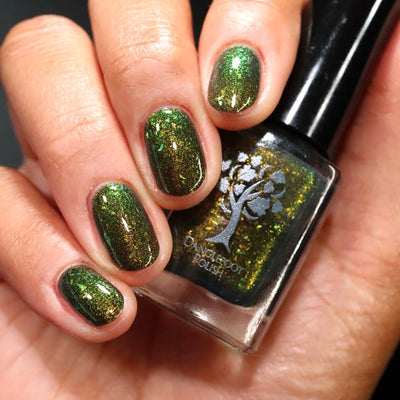 Succumb to the Fear by Danglefoot Nail Polish, black-gold multichrome shimmer flakie thermal bottle held in a light-medium hand