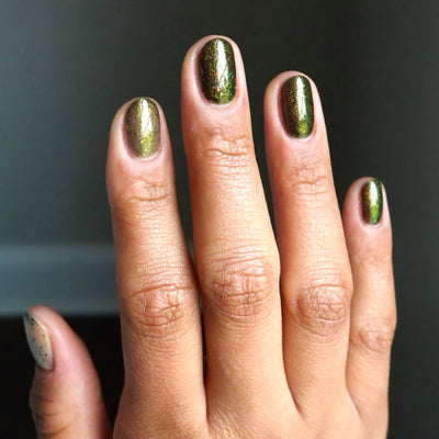 Succumb to the Fear by Danglefoot Nail Polish, black-gold multichrome shimmer flakie thermal on a medium skin tone hand