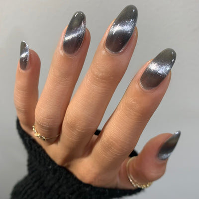 Amulet by Starrily, silver foil magnetic topper with linear cat-eye shimmer stripe over a deep charcoal grey base, on a light-medium skin tone hand