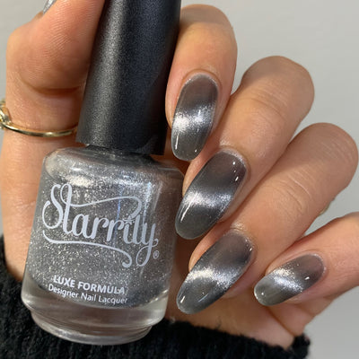 Amulet by Starrily, silver foil magnetic topper with pronounced linear cat-eye streak over a cool grey base, bottle held in a light-medium hand