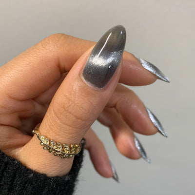 Amulet by Starrily, silver foil magnetic topper with dramatic 3D cat-eye pull, deep charcoal shadow and bright silver shimmer highlights, on a medium skin tone hand