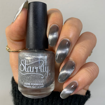 Amulet by Starrily, silver foil magnetic topper with bright silver cat-eye streak pulled across a charcoal grey base, bottle held in a light-medium hand