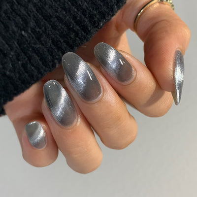 Amulet by Starrily, silver foil magnetic topper with 3D cat-eye effect, silver shimmer streaking across a steel grey base with deep shadow zones, on a light-medium skin tone hand