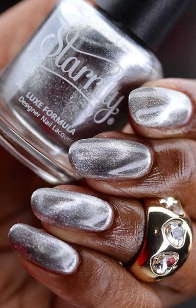 Amulet by Starrily, silver chrome magnetic topper showing dramatic 3D wave pattern with chrome highlight peaks and shadowed pull zones, bottle held in a rich hand