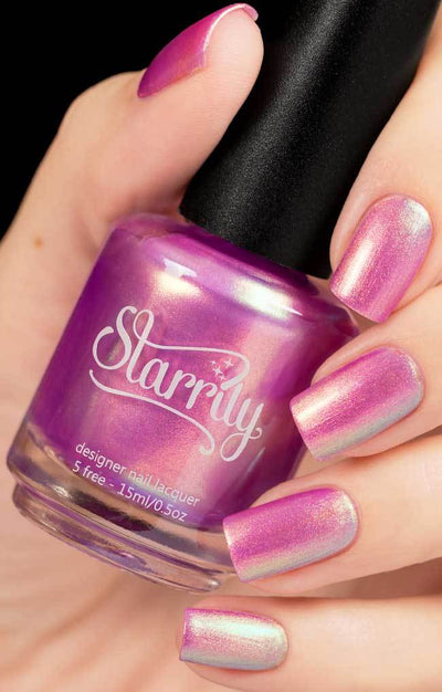 Aphrodite by Starrily, pink-magenta foil-like shimmer metallic with green-to-blue color-shifting, bottle held in a light skin tone hand