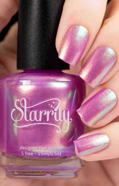 Aphrodite by Starrily, vivid magenta-pink shimmer metallic with pink-to-green-to-blue foil shift, bottle held in a light skin tone hand