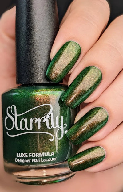 Artemis by Starrily, forest green shimmer with copper and gold-green shift, linear cat-eye effect visible under studio light, bottle held in a light hand