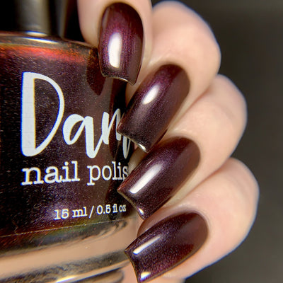 Change of Heart by Dam Nail Polish, blackened red multichrome shifting to burnt orange on four stiletto nails, on a light skin tone hand
