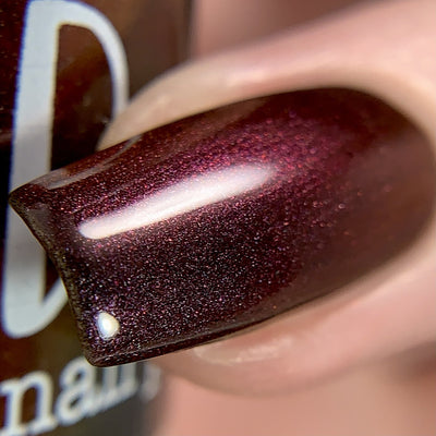 Change of Heart by Dam Nail Polish, black-red multichrome with vivid red-to-orange microflake shift under direct flash, on a light skin tone hand
