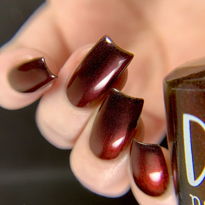 Change of Heart by Dam Nail Polish, vampy black-red multichrome showing deep crimson shimmer with darkened shadow zones, on a light skin tone hand