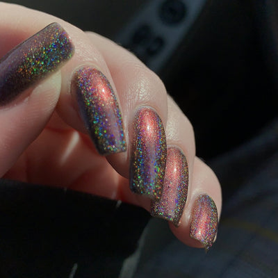 Change of Heart (Holo) by Dam Nail Polish, dark black-red base shifting to warm orange with fine holographic scatter in indoor warm light, on a light skin tone hand