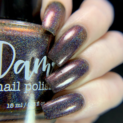 Change of Heart (Holo) by Dam Nail Polish, dark reddish-brown holographic multichrome showing vivid red-to-copper-orange shift with linear holo shimmer, on a light skin tone hand