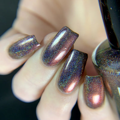 Change of Heart (Holo) by Dam Nail Polish, blackened burgundy-red holographic multichrome shifting to amber-orange with high-gloss linear holo shimmer, on a light skin tone hand