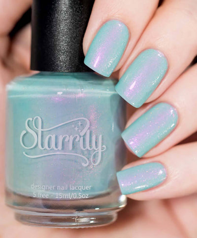 Clockwork Roses by Starrily, seafoam mint creme showing vivid pink-to-purple iridescent shimmer shift with holographic micro flecks, bottle held in a light skin tone hand
