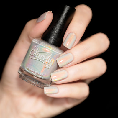 Daisy by Starrily, sheer white-grey base showing vivid orange-gold shimmer flare, bottle held in a light hand