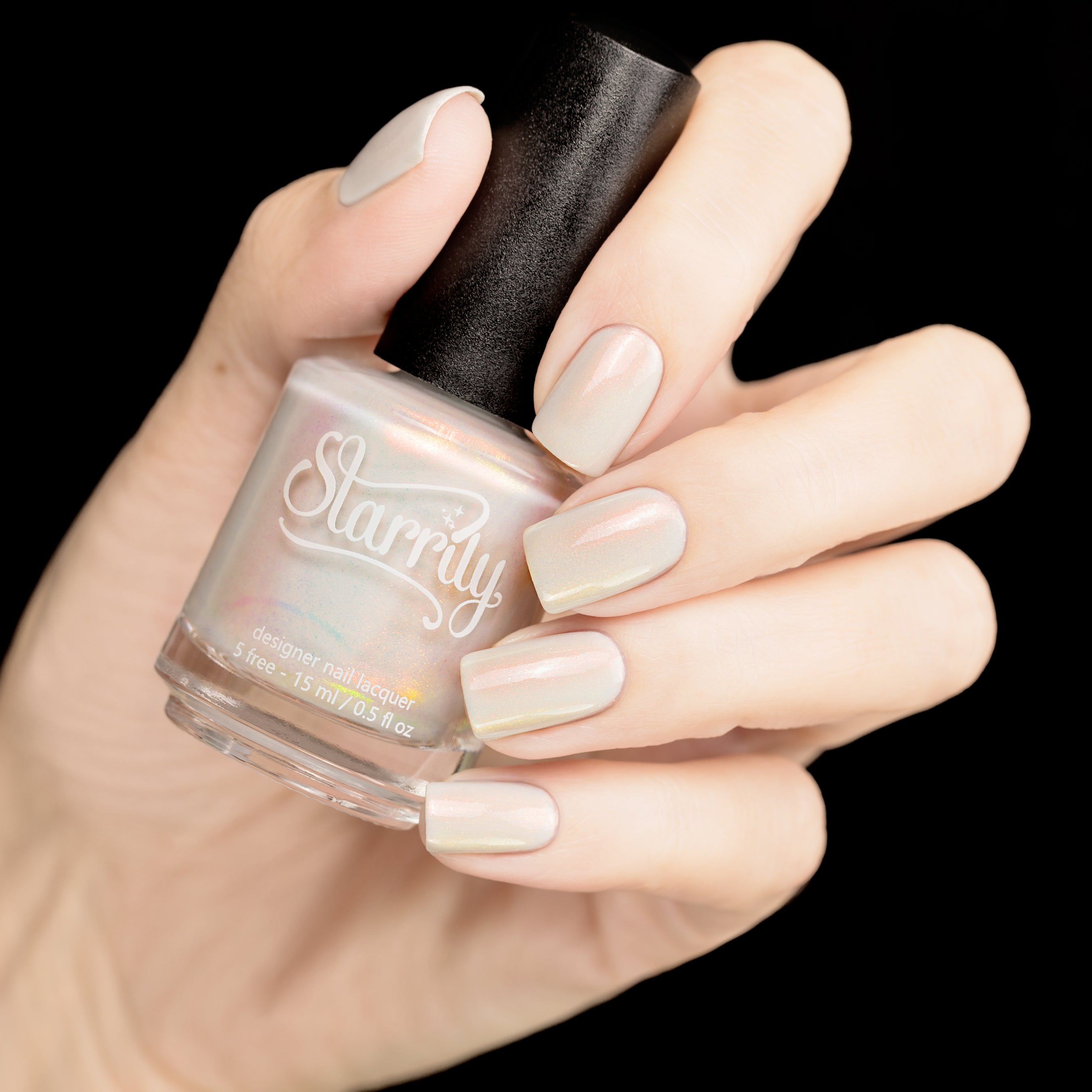 Daisy by Starrily, sheer white-grey base with pearlescent aurora shimmer in muted resting state, bottle held in a light hand