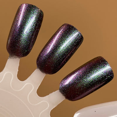Distant Dimensions by Dam Nail Polish, deep plum-black base with green magnetic streaks and purple-pink multichrome shift, swatch stick