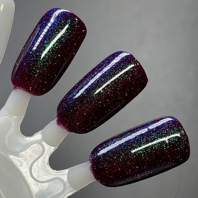 Murder Manor by Dam Nail Polish, deep maroon base with blue-green shimmer shift and scattered red holographic sparkle, swatch stick