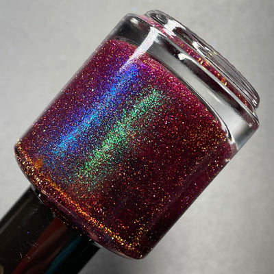 Murder Manor by Dam Nail Polish, deep maroon with vivid blue-green shimmer shift and scattered red and gold reflective glitter, bottle standalone product shot