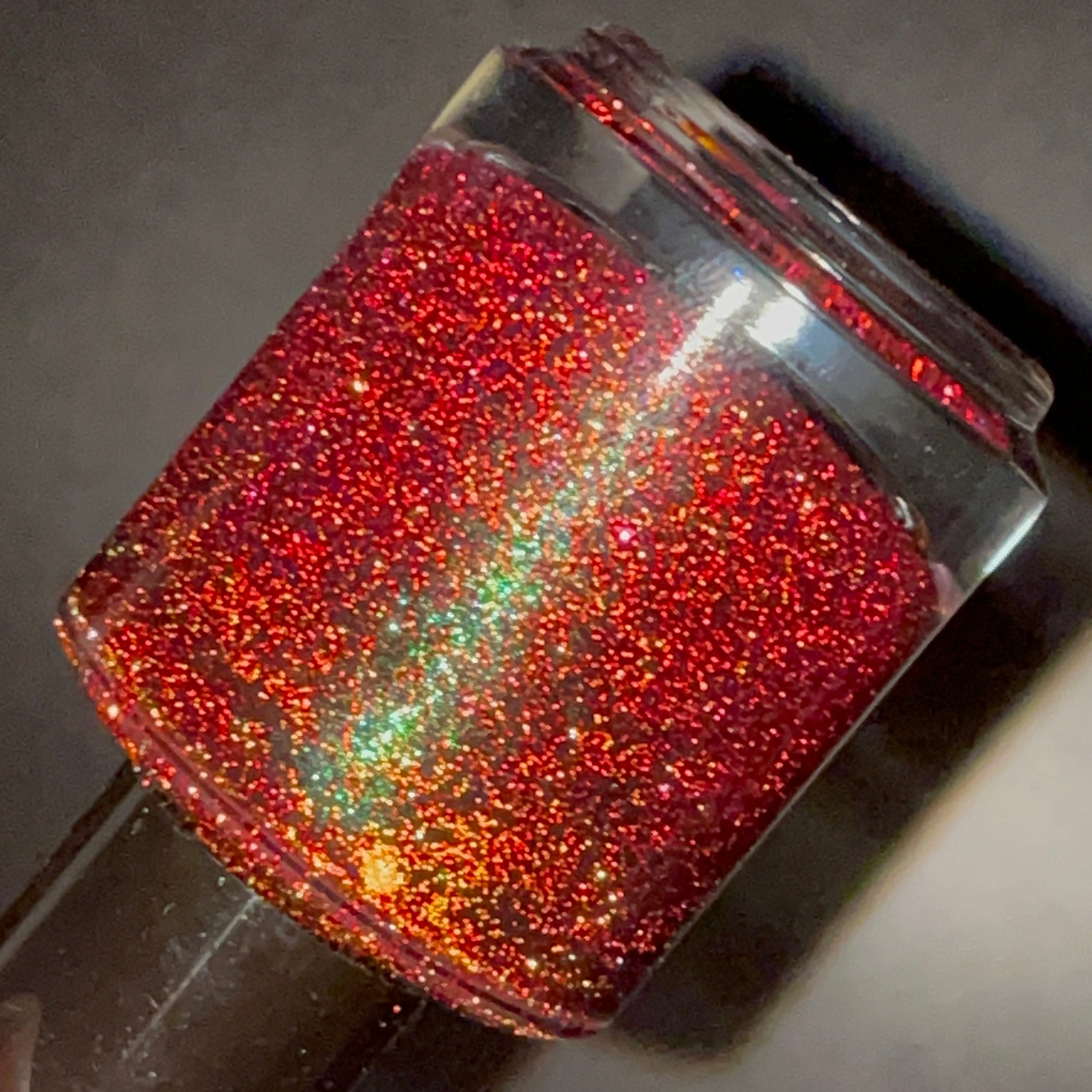 Murder Manor by Dam Nail Polish, deep maroon-red base packed with red and gold micro-glitter showing green-blue shimmer shift, bottle standalone product shot