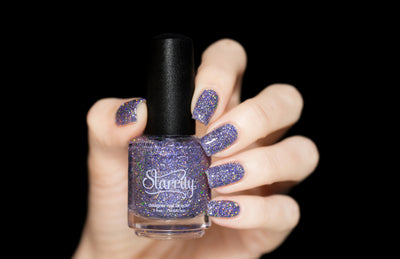Damsel by Starrily, lilac holographic glitter in clear base showing intense rainbow scatter under direct flash, bottle held in a light hand