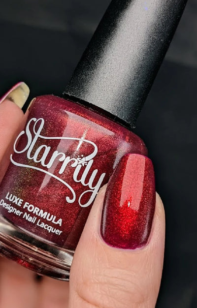 Dragon by Starrily, deep crimson-red copper shimmer shift over dark burgundy-purple base, bottle held in a light hand