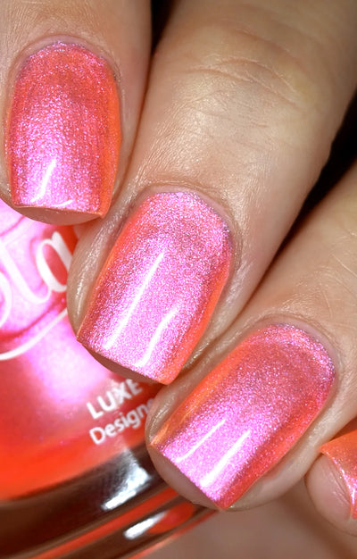 Moon Sugar by Starrily, vivid hot pink to coral-orange color shift with fine metallic shimmer particles in bright daylight, on a light-medium skin tone hand