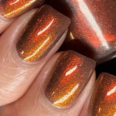 Dingle Berries by Dam Nail Polish, deep brown base with fiery red-orange to bronze-gold shimmer shift in bright daylight, on a light skin tone hand