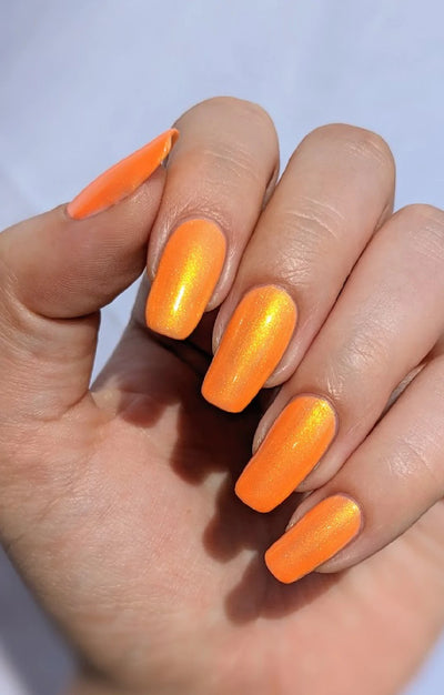 Peach Glow by Starrily, neon orange base with gold-to-green color-shifting shimmer in bright daylight, on a light-medium skin tone hand