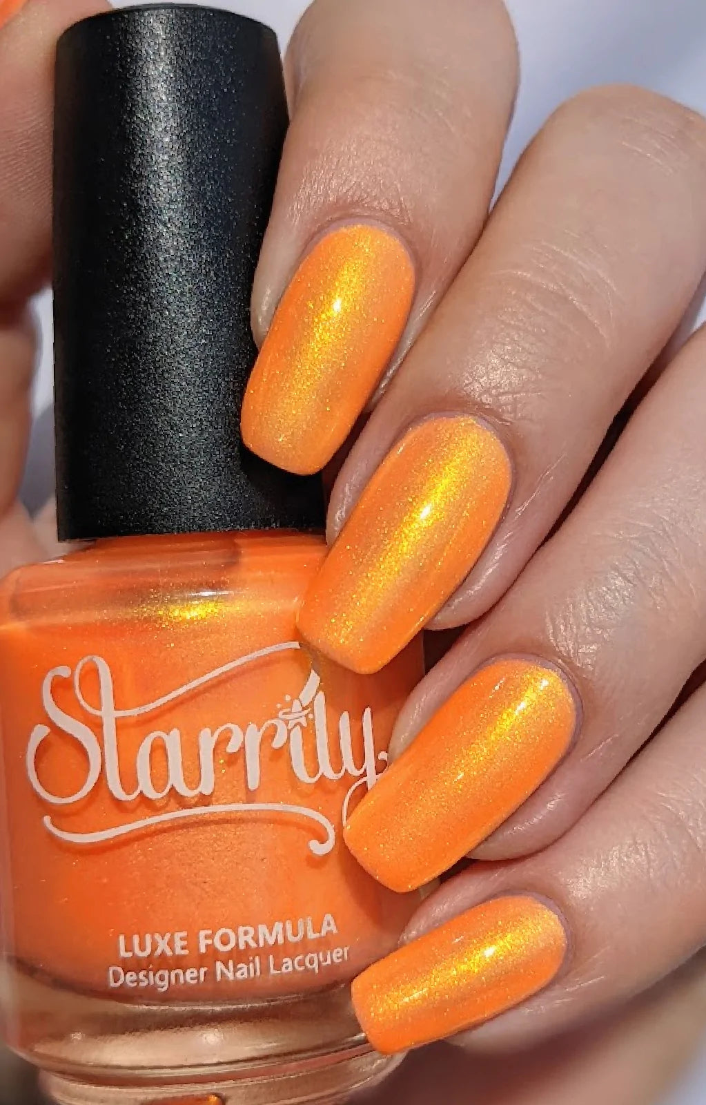 Peach Glow by Starrily, vivid orange base showing strong gold and green duochrome shimmer shift in daylight, bottle held in a light hand